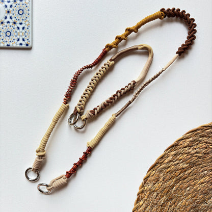 Three braided crossbody straps in beige, brown, and red on a white surface with a woven mat