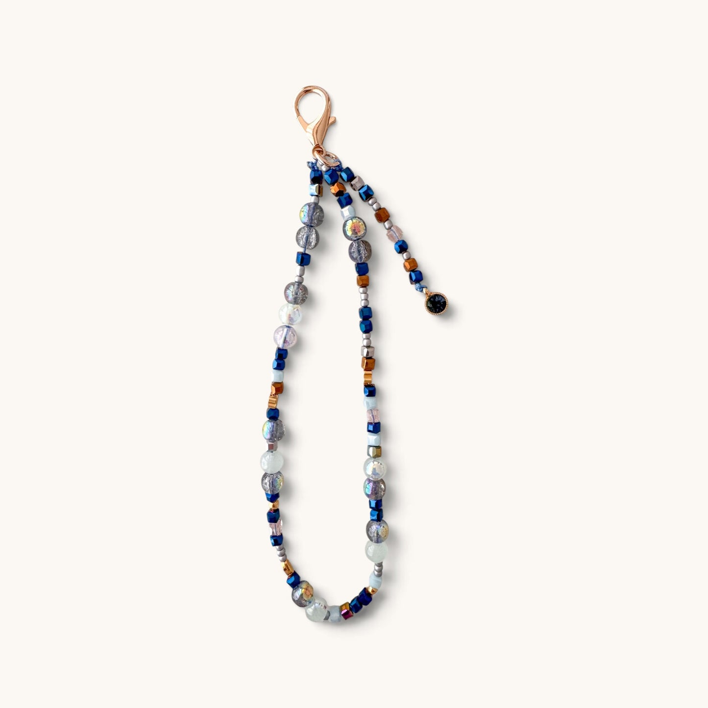 A beaded phone strap featuring a mix of blue, gray, white, and amber glass beads with a rose gold clasp, shown against a plain off-white background.