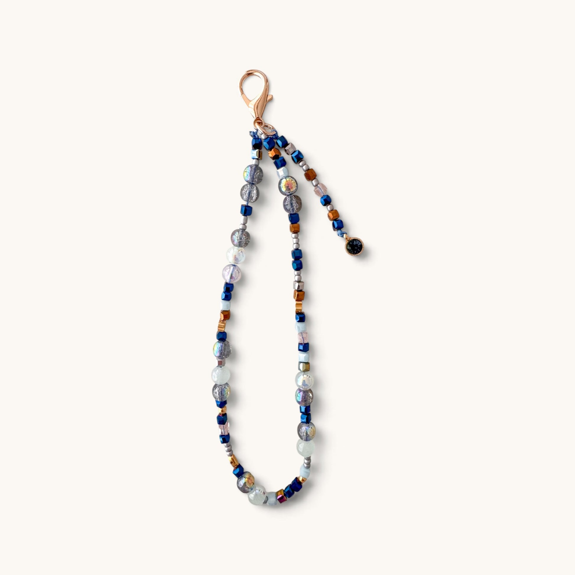 A beaded phone strap featuring a mix of blue, gray, white, and amber glass beads with a rose gold clasp, shown against a plain off-white background.