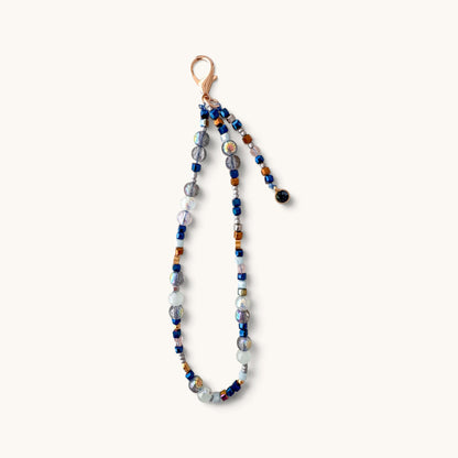 A beaded phone strap featuring a mix of blue, gray, white, and amber glass beads with a rose gold clasp, shown against a plain off-white background.