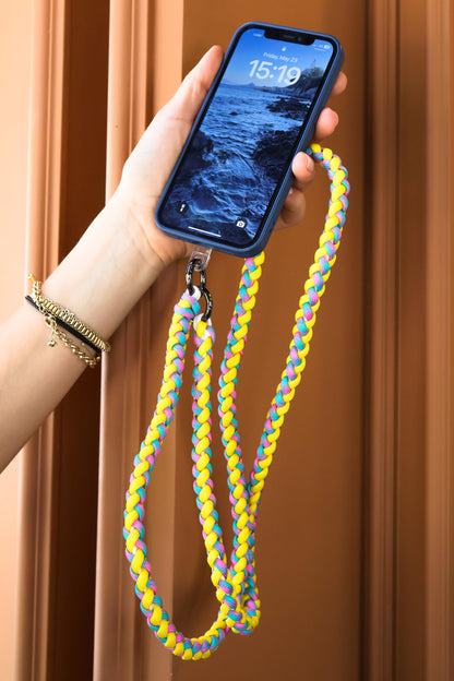 Hand holding a phone with Citrus Twist macrame crossbody strap with phone against a wooden background