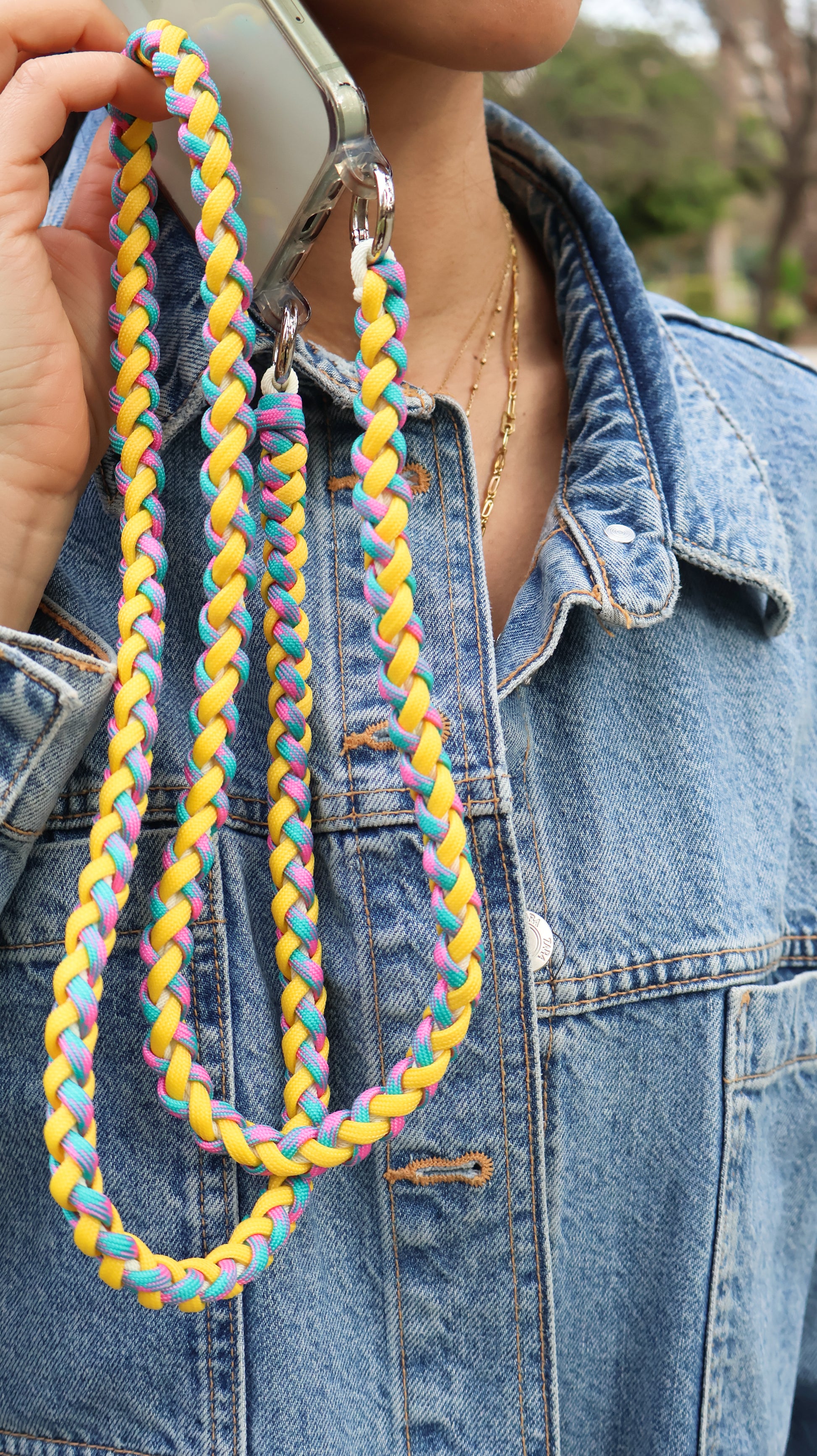 Citrus Twist hand-knotted macrame crossbody strap holding a colorful braided lanyard against a denim jacket background