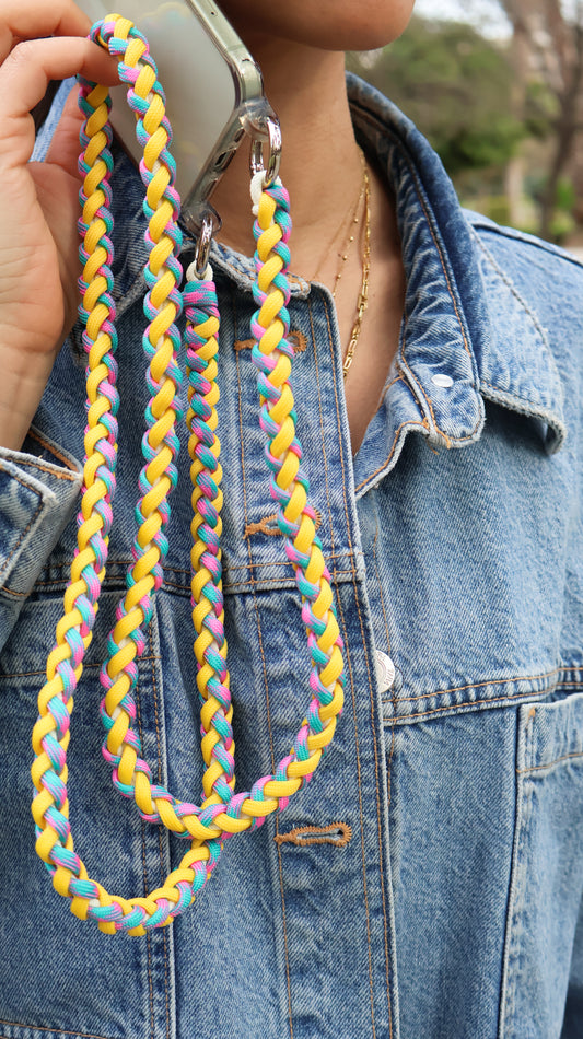 Citrus Twist hand-knotted macrame crossbody strap holding a colorful braided lanyard against a denim jacket background