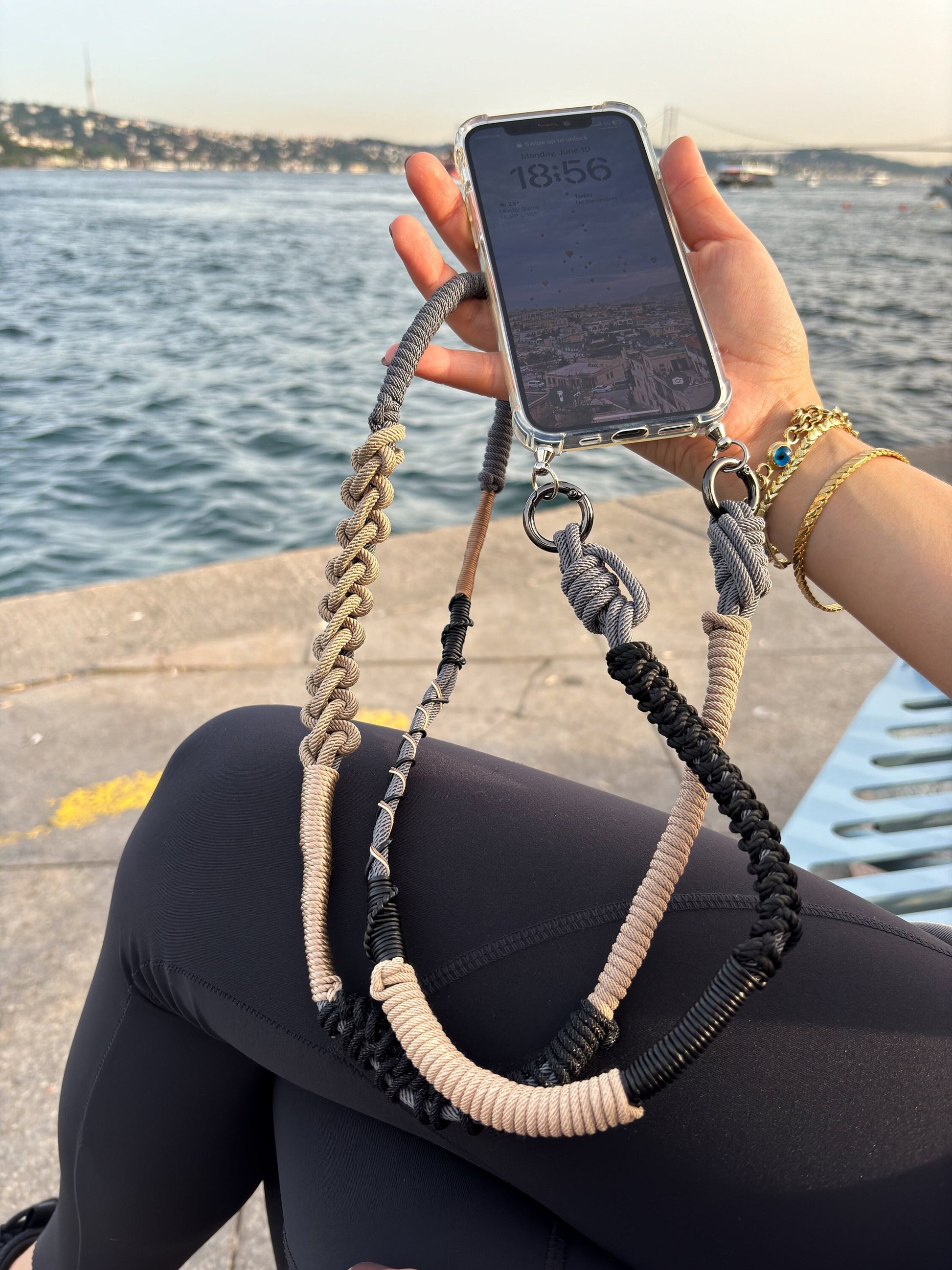 Person holding a phone with Granite Shore crossbody strap by a waterfront