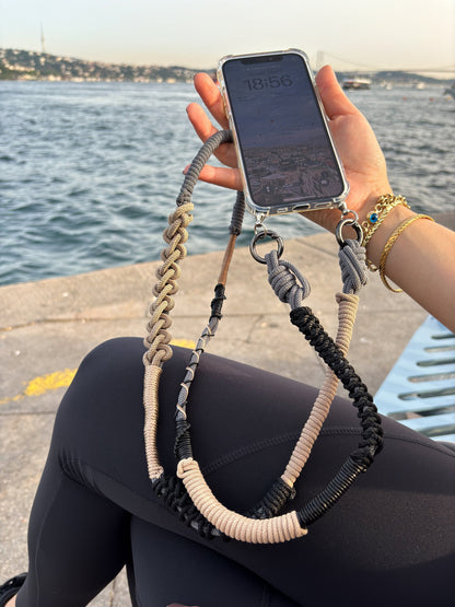 Person holding a phone with Granite Shore crossbody strap by a waterfront