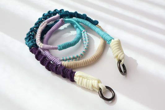 Hand-knotted multicolor braided phone strap in navy, teal, lilac, and cream, shown attached to a phone case with gold clasp hardware