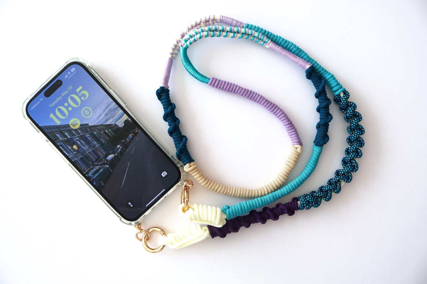 Hand-knotted multicolor braided phone strap in navy, teal, lilac, and cream, shown attached to a phone case with gold clasp hardware