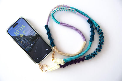 Hand-knotted multicolor braided phone strap in navy, teal, lilac, and cream, shown attached to a phone case with gold clasp hardware