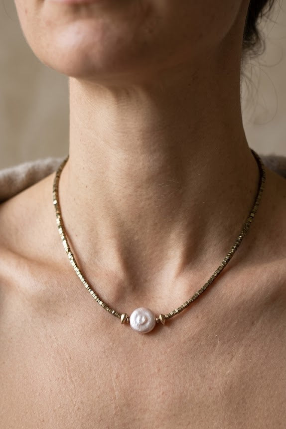A close-up of a model wearing a delicate gold chain necklace with a single white pearl pendant.