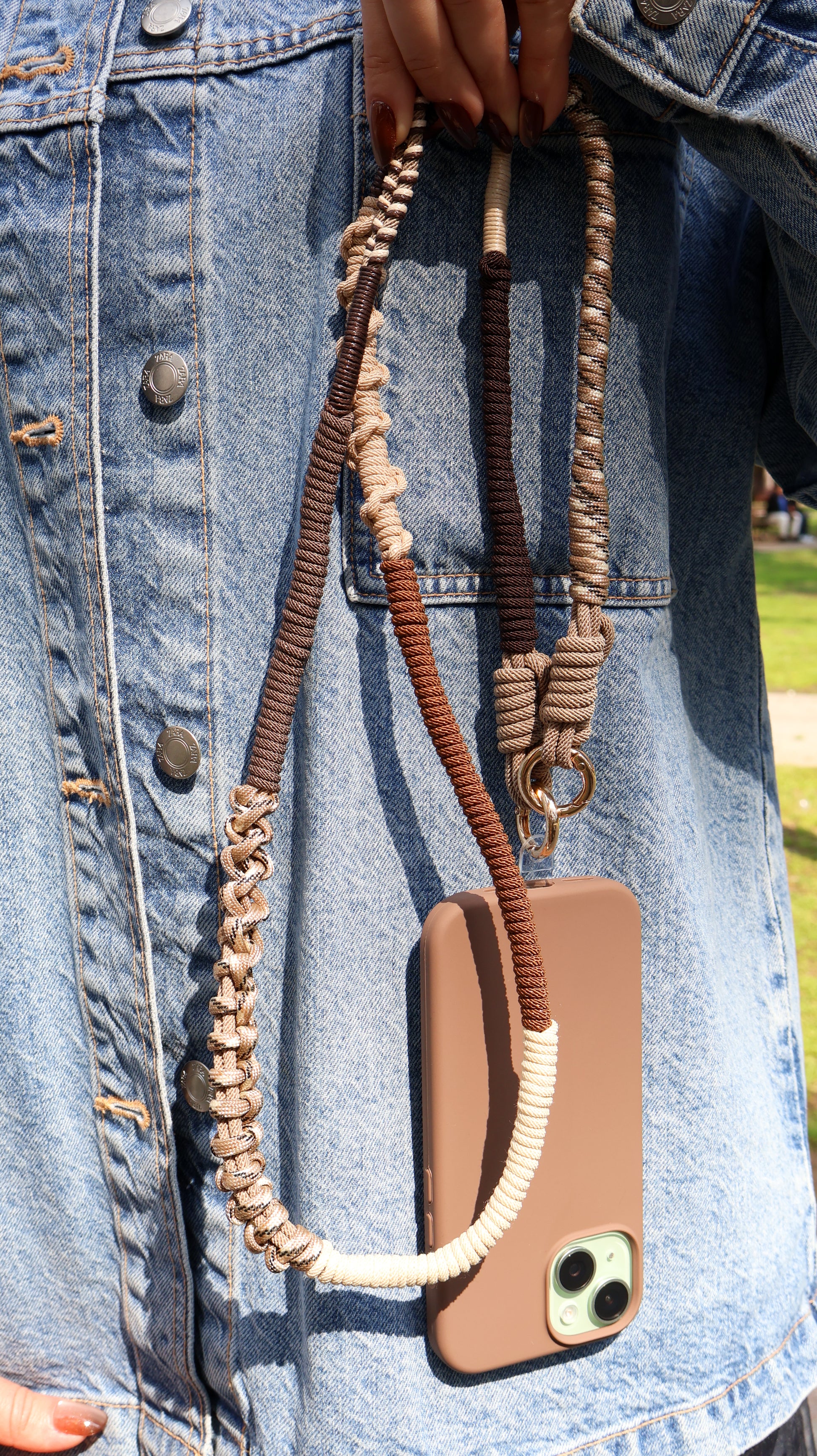 Phone case with Sienna Ridge macrame crossbody strap held by a person wearing a denim jacket.