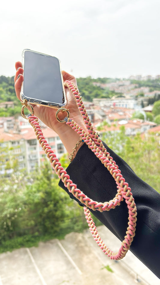 Person holding a phone with a pink braided strap against a scenic background