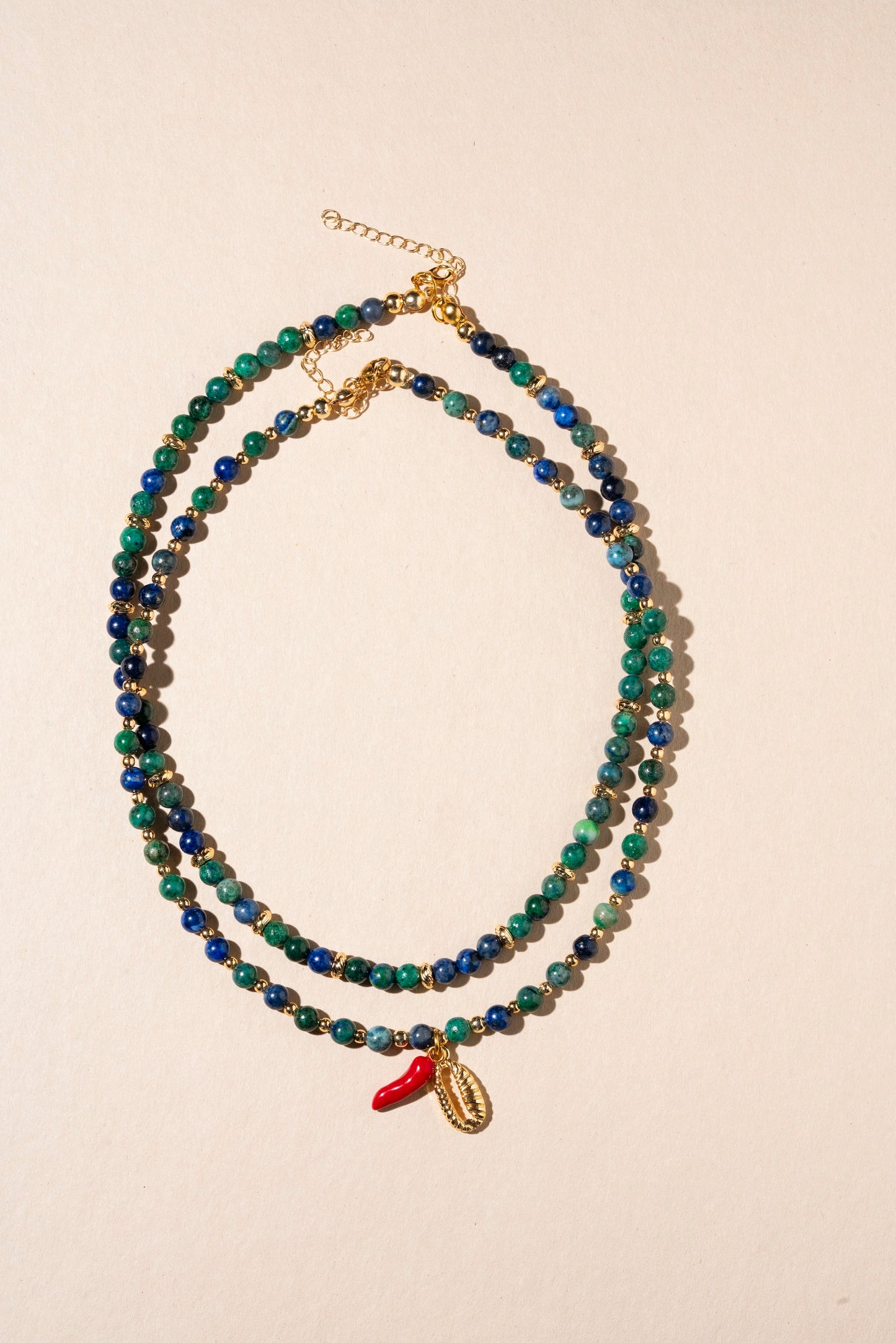 Beaded necklace with a small red charm on a beige background
