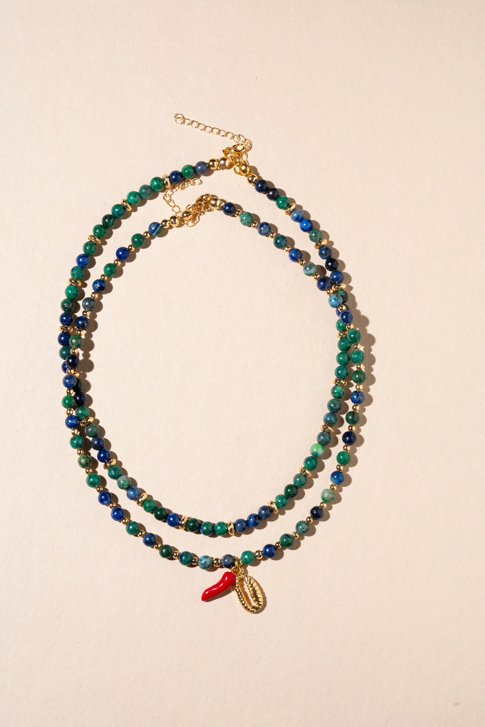 Beaded necklace with a small red charm on a beige background