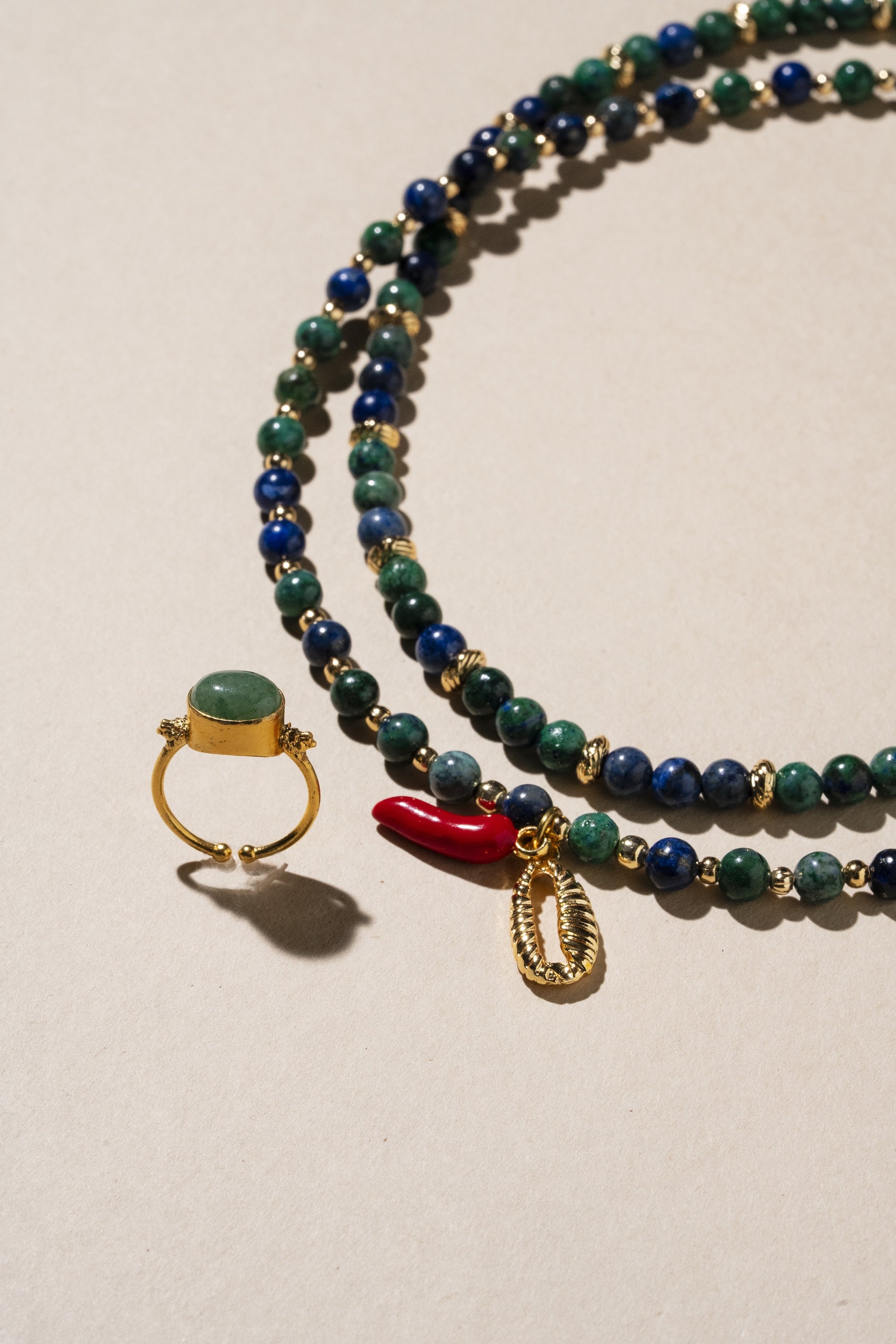Beaded necklace with a ring and coral charm on a beige background