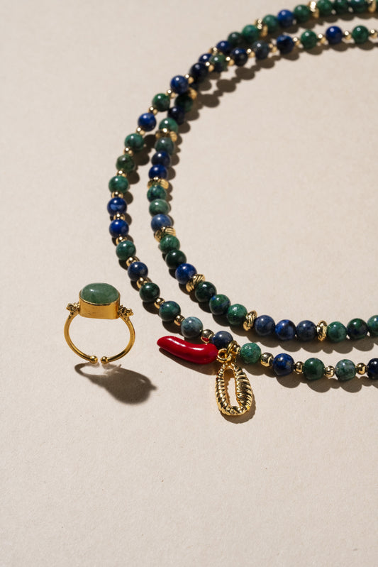 Beaded necklace with a ring and coral charm on a beige background