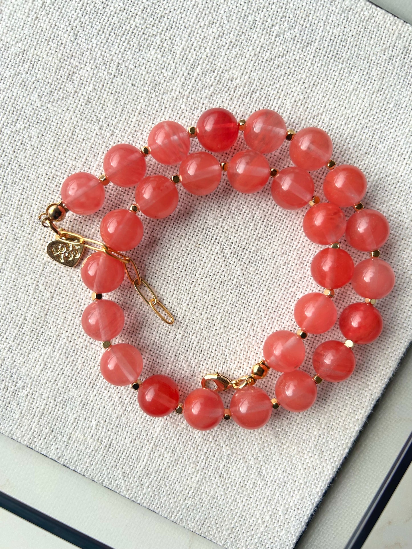 Pink beaded bracelet with gold accents on a textured surface