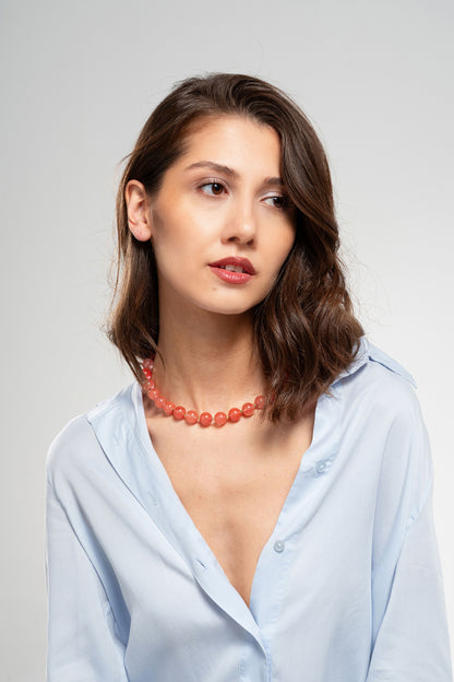 Woman wearing a light blue shirt and red necklace against a gray background