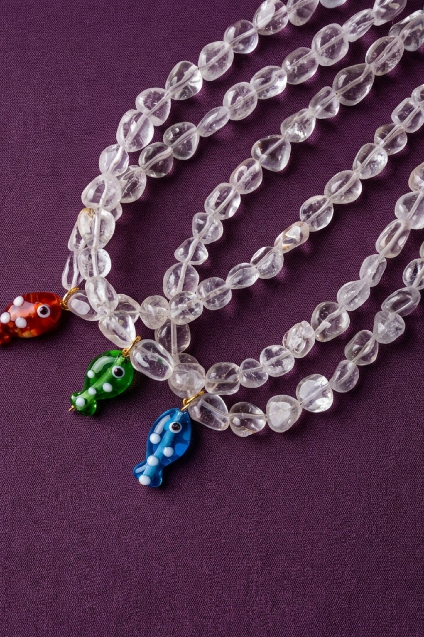 Clear beaded necklace with colorful fish charms on a purple background