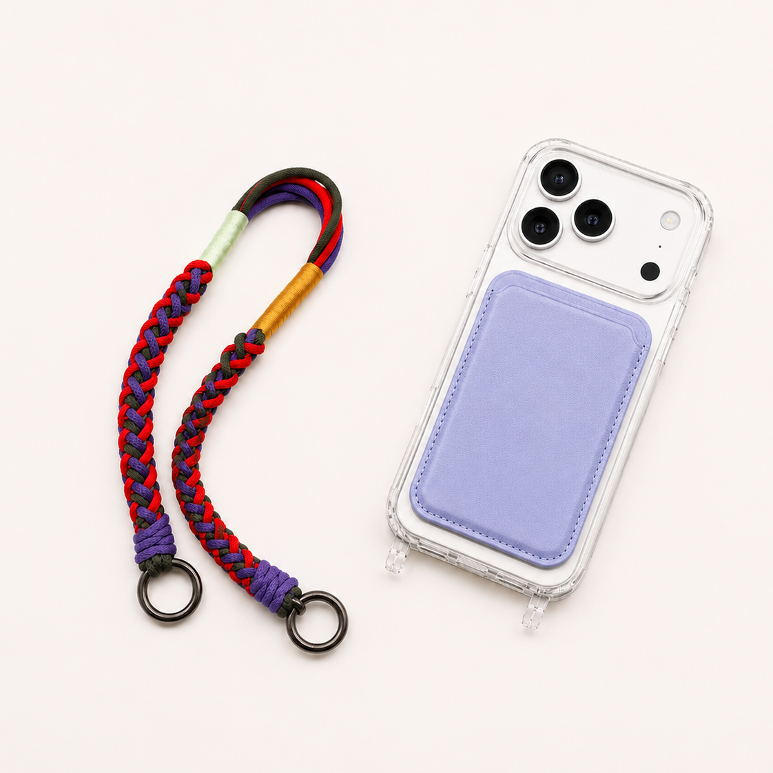 White iPhone 17 Pro in a clear MagSafe case with a lavender card holder and colorful braided wristlet strap on a warm off-white background.