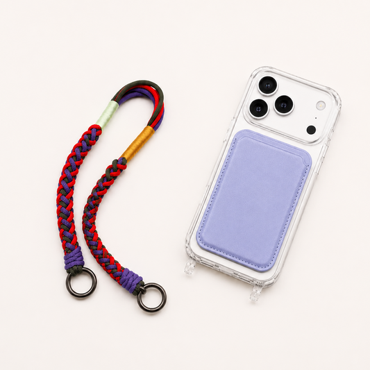 White iPhone 17 Pro in a clear MagSafe case with a lavender card holder and colorful braided wristlet strap on a warm off-white background.